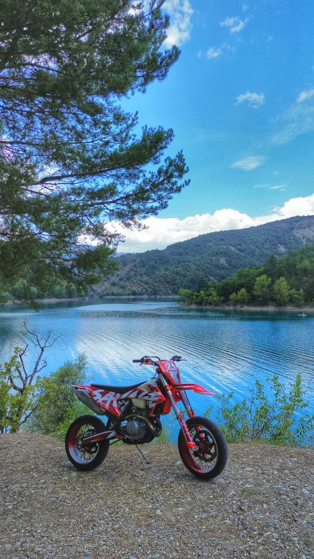 Moto supermotard rouge à l'arrêt devant un lac de montagne